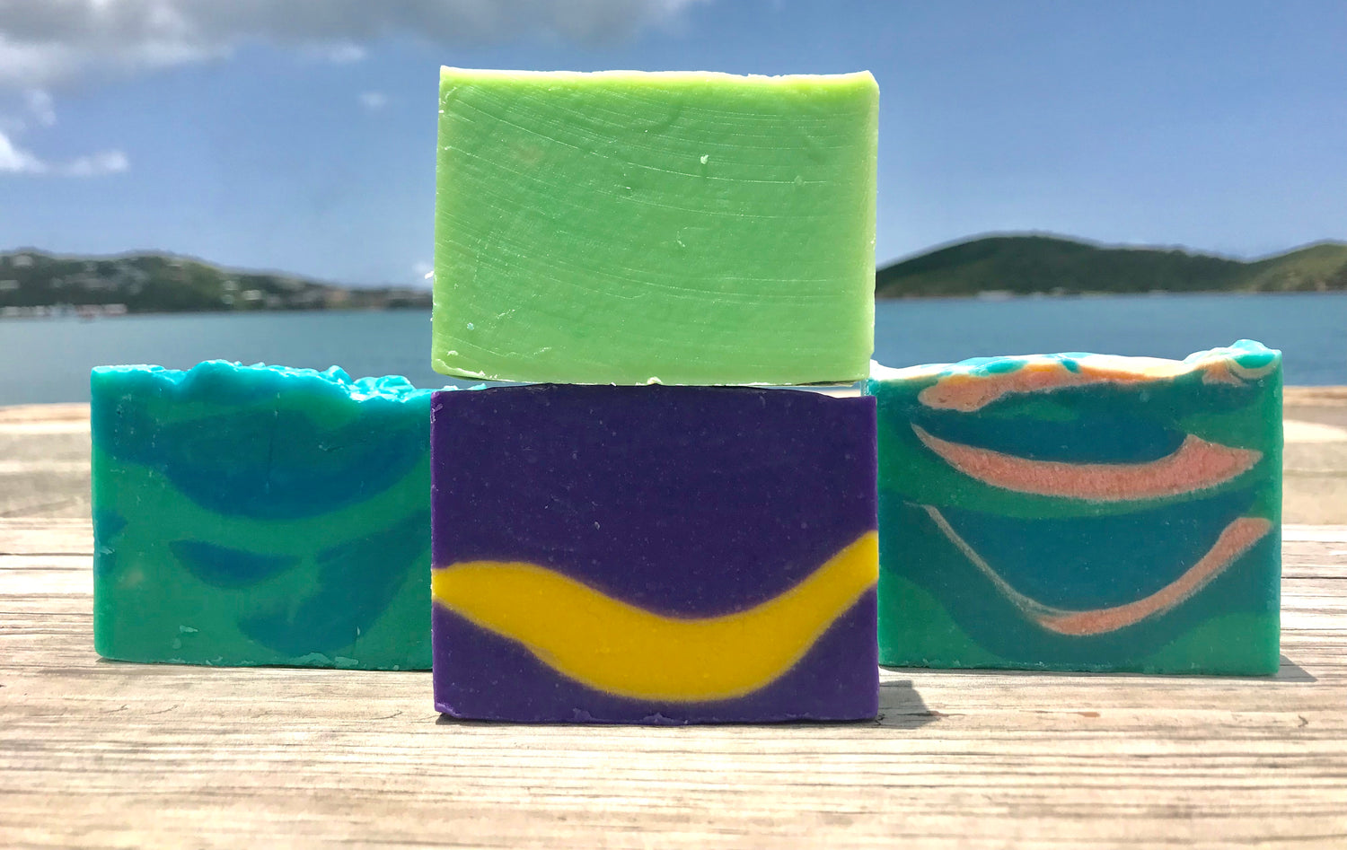 ocean themed or colorful handmade soaps by JDNatlady's Creations on light wooden surface with water and islands in background 